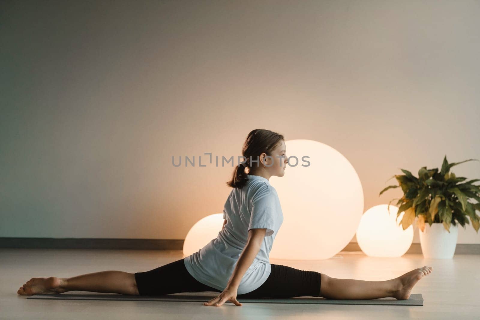 A teenage girl in sports clothes does yoga in a fitness room.