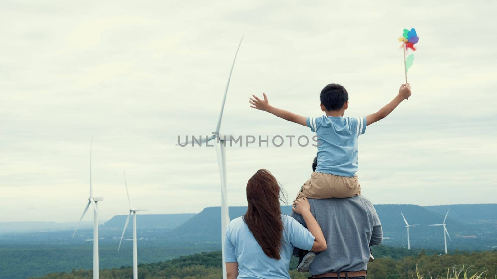 Concept of progressive happy family enjoying their time at the wind turbine farm. Electric generator from wind by wind turbine generator on the country side with hill and mountain on the horizon.