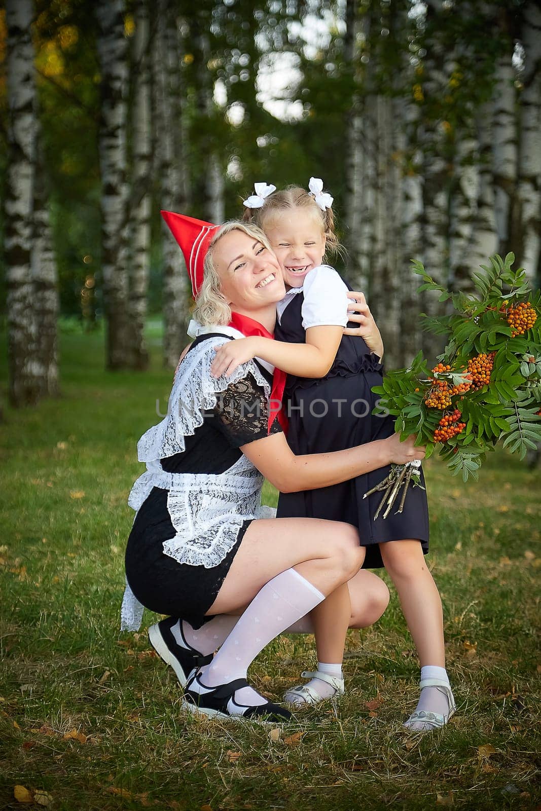 Young and adult schoolgirl on September 1 with flowers. Generations of schoolchildren of USSR and Russia. Female pioneer in red tie and October girl in modern uniform. Mother and daughter having fun by keleny