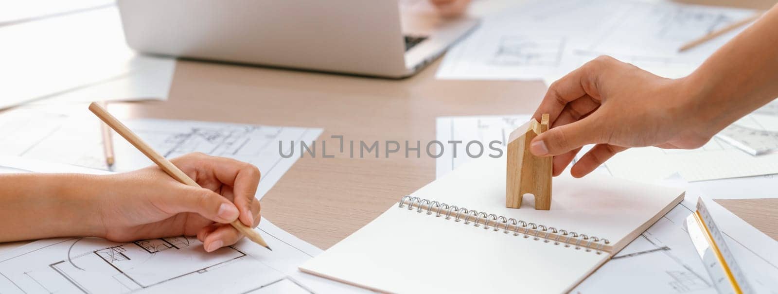 Professional architect hand draws a blueprint on table with architectural document and wooden block scatter around at office. Design and Planing concept. Focus on hand. Closeup. Delineation.