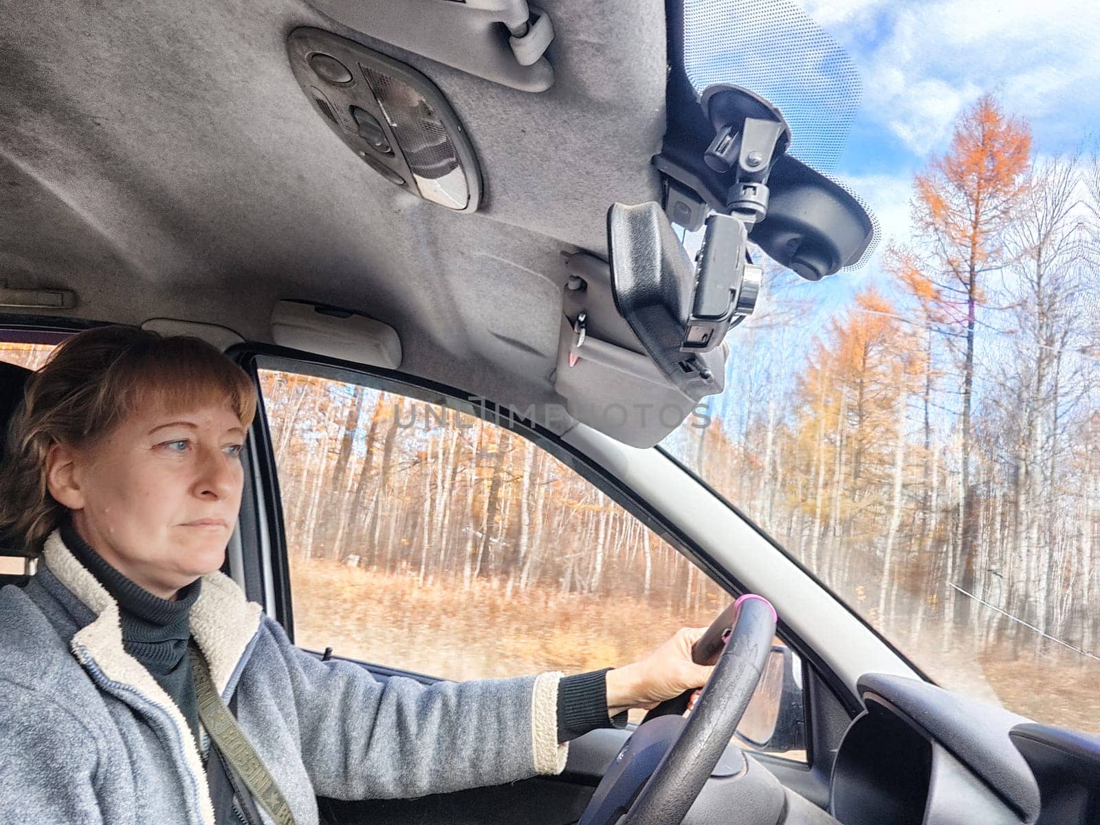 Portrait of female driver in solo journey. Adult mature woman holding steering wheel and looking through windscreen in travel by vehicle on vacation. Lady girl who is owner or rent a car for travel by keleny