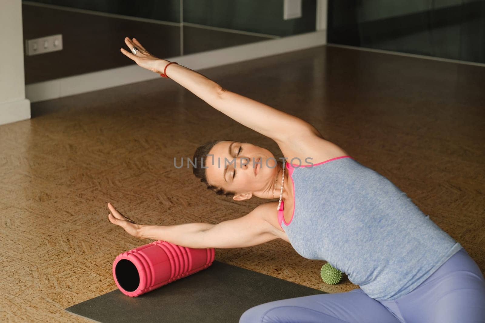 Slender girl doing yoga with a big massage roller on the floor.