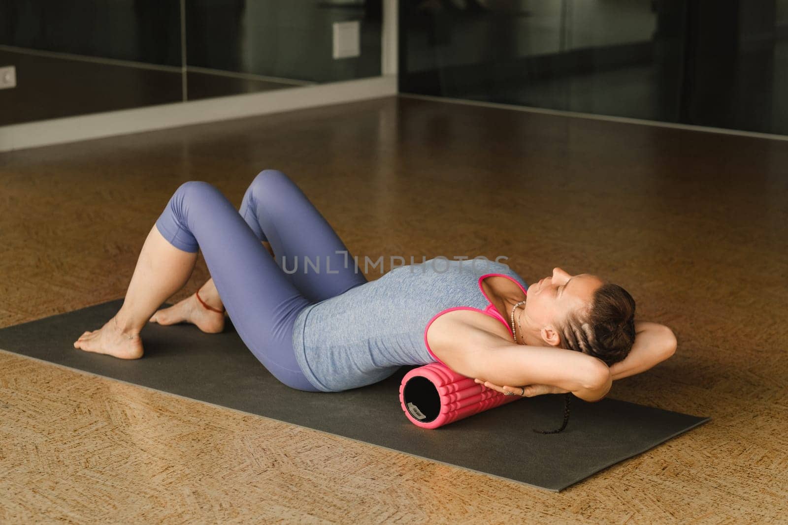 Slender girl doing yoga with a big massage roller on the floor by Lobachad