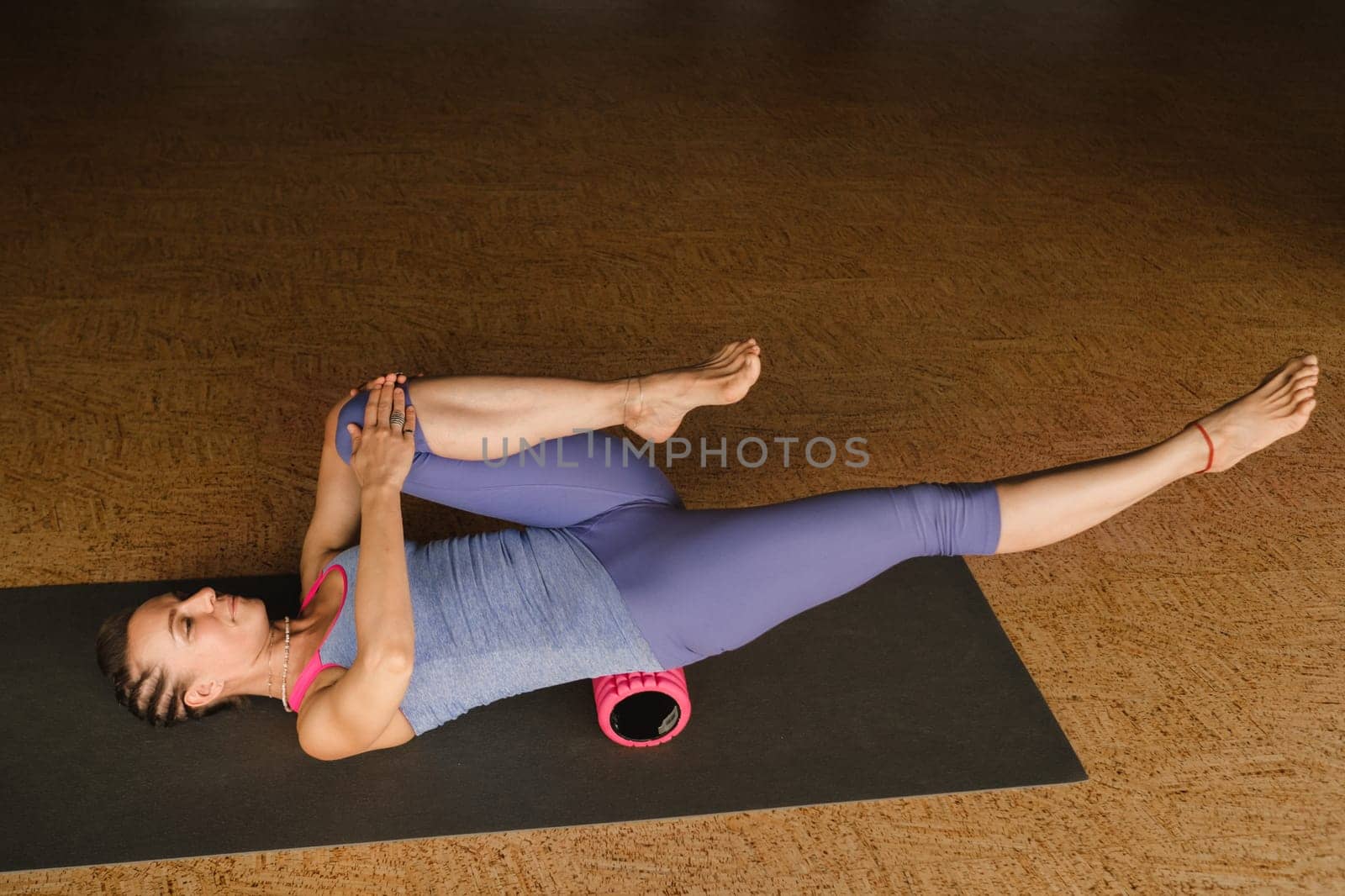 Slender girl doing yoga with a big massage roller on the floor by Lobachad