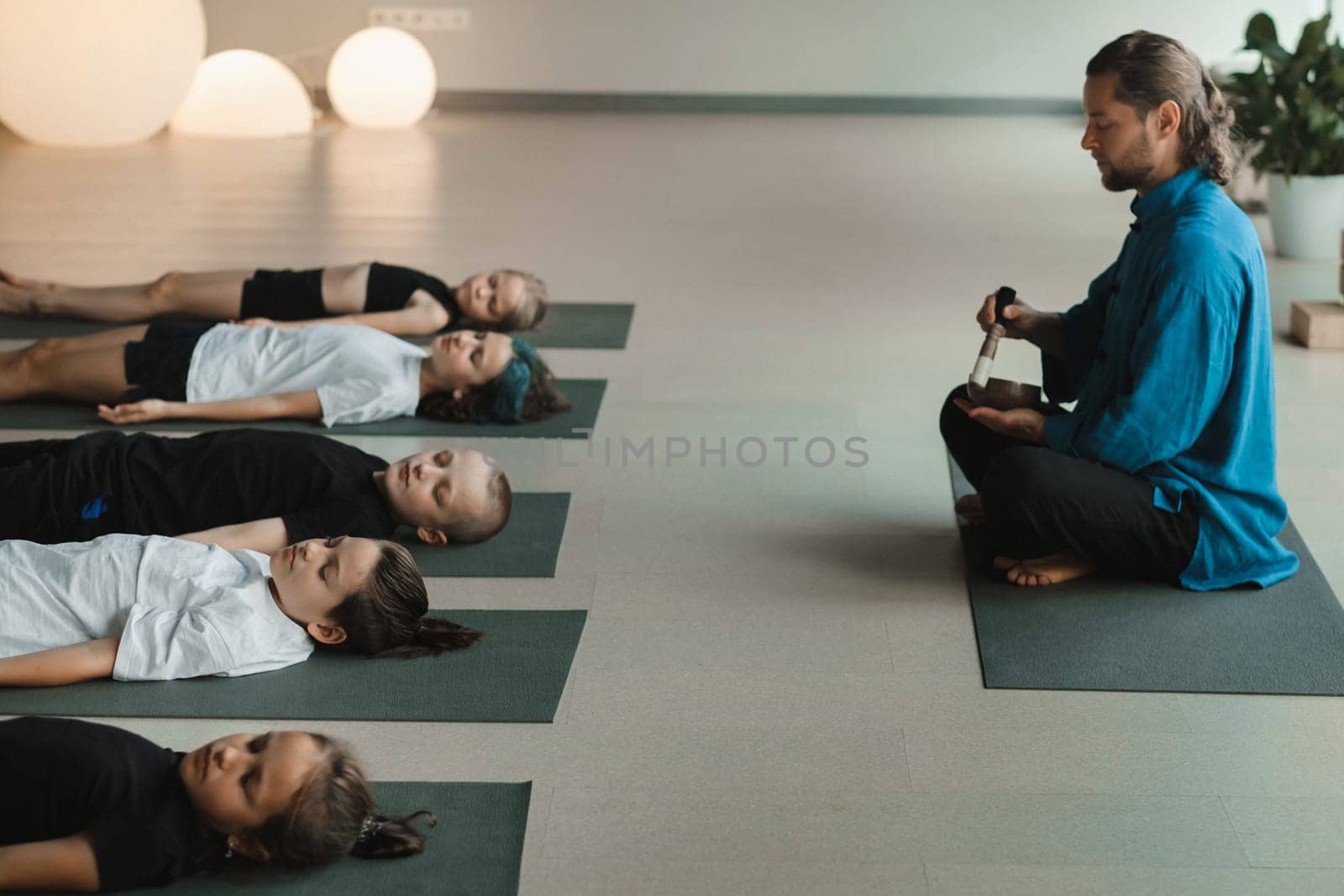 Children relax lying down to the sounds of a Tibetan bowl in the fitness room. Children's yoga.