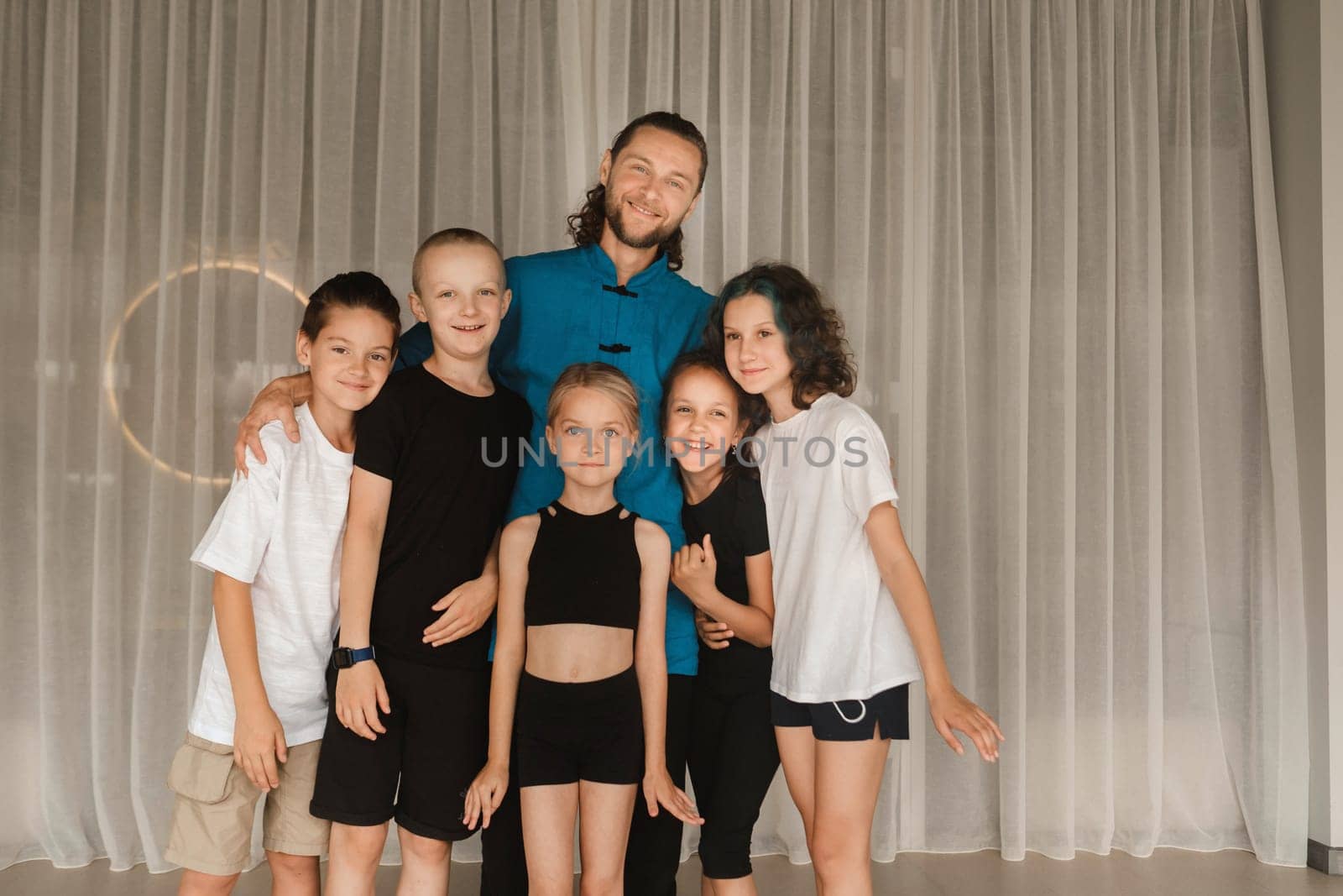 A joint portrait of a yoga coach and children standing in a fitness room.