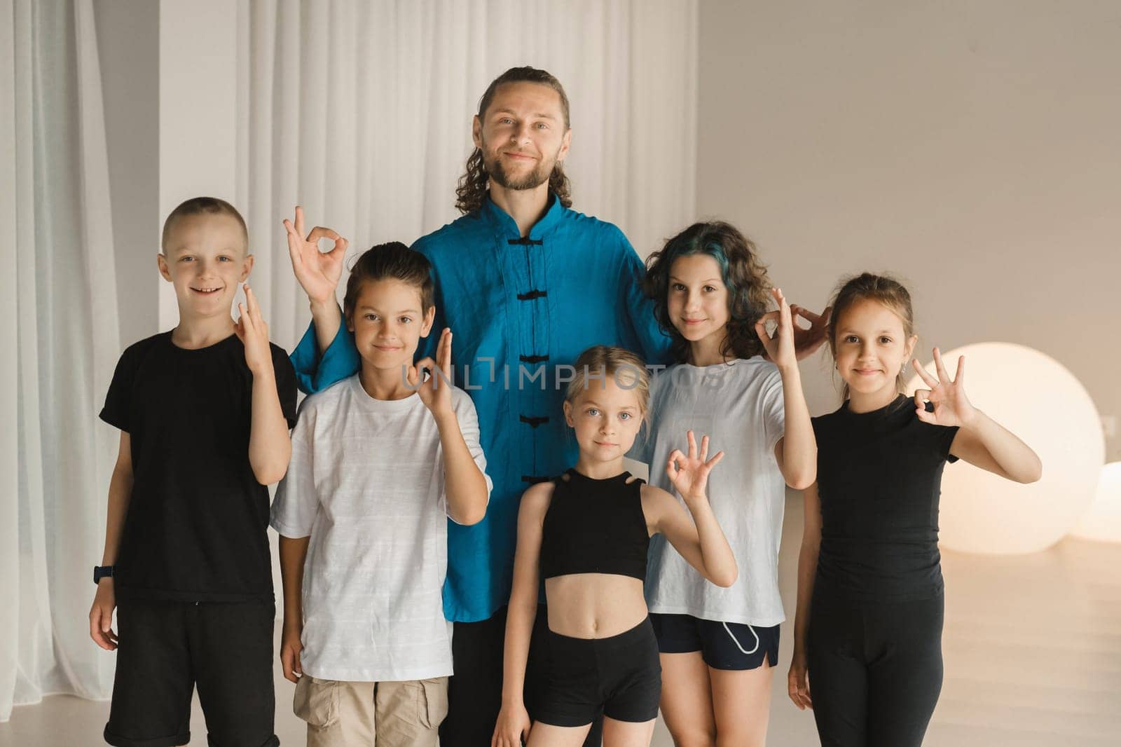 A joint portrait of a yoga coach and children standing in a fitness room.