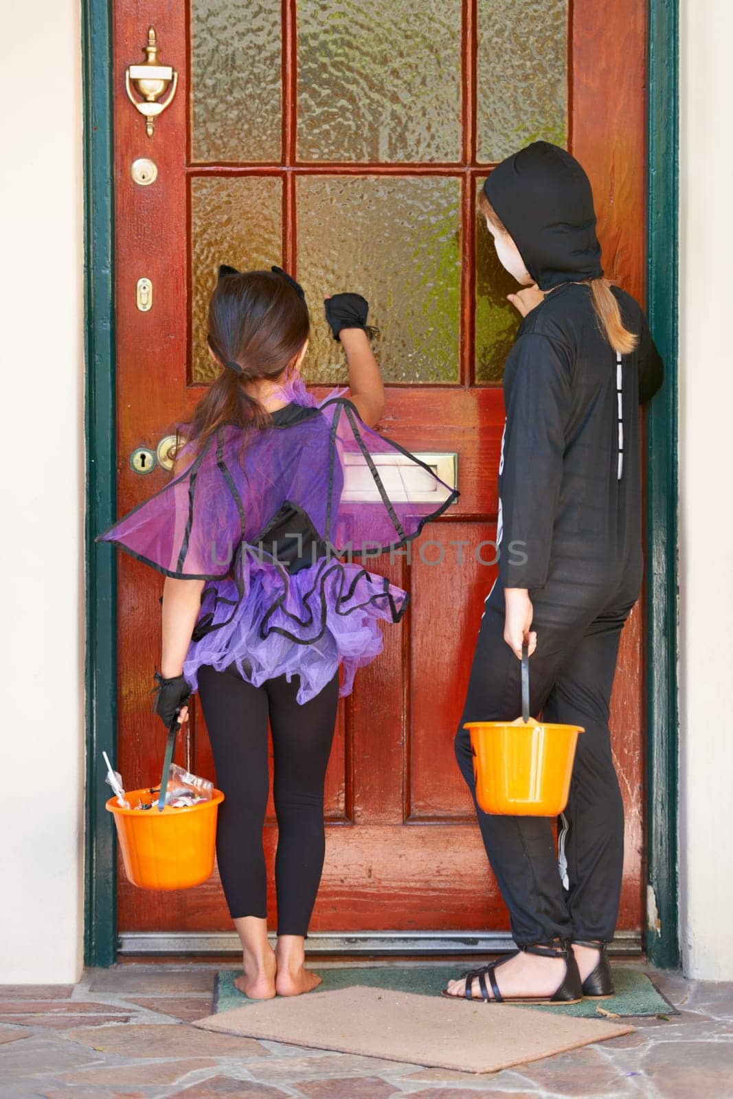 Tick or treating is so much fun. Rearview shot of some children knocking on a door during halloween. by YuriArcurs
