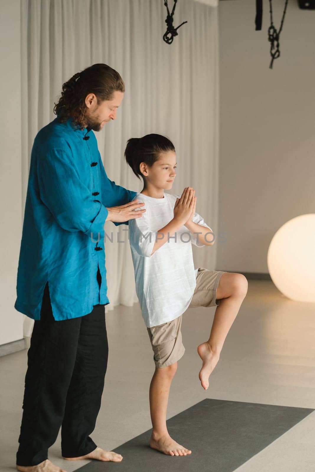 A yoga instructor in training helps a child to do exercises in the gym by Lobachad