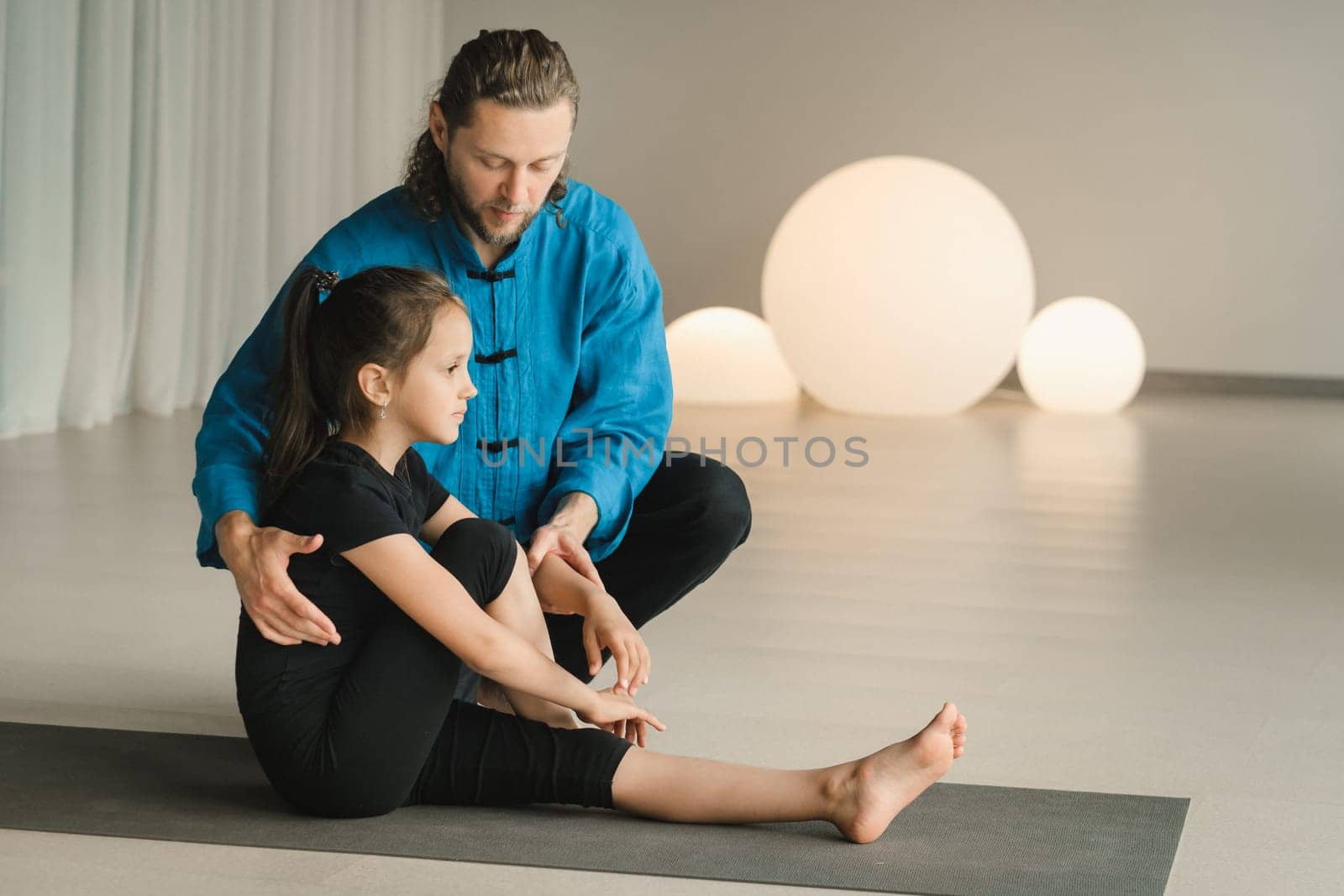 A yoga instructor in training helps a child to do exercises in the gym by Lobachad