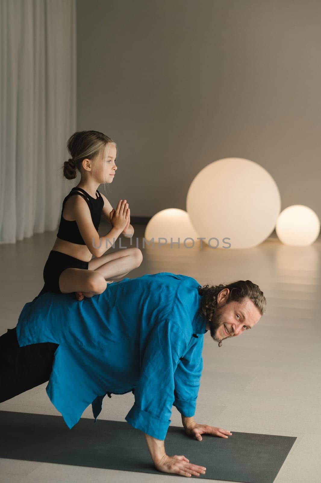 a child in the lotus position sits on the back of a yoga coach during training.