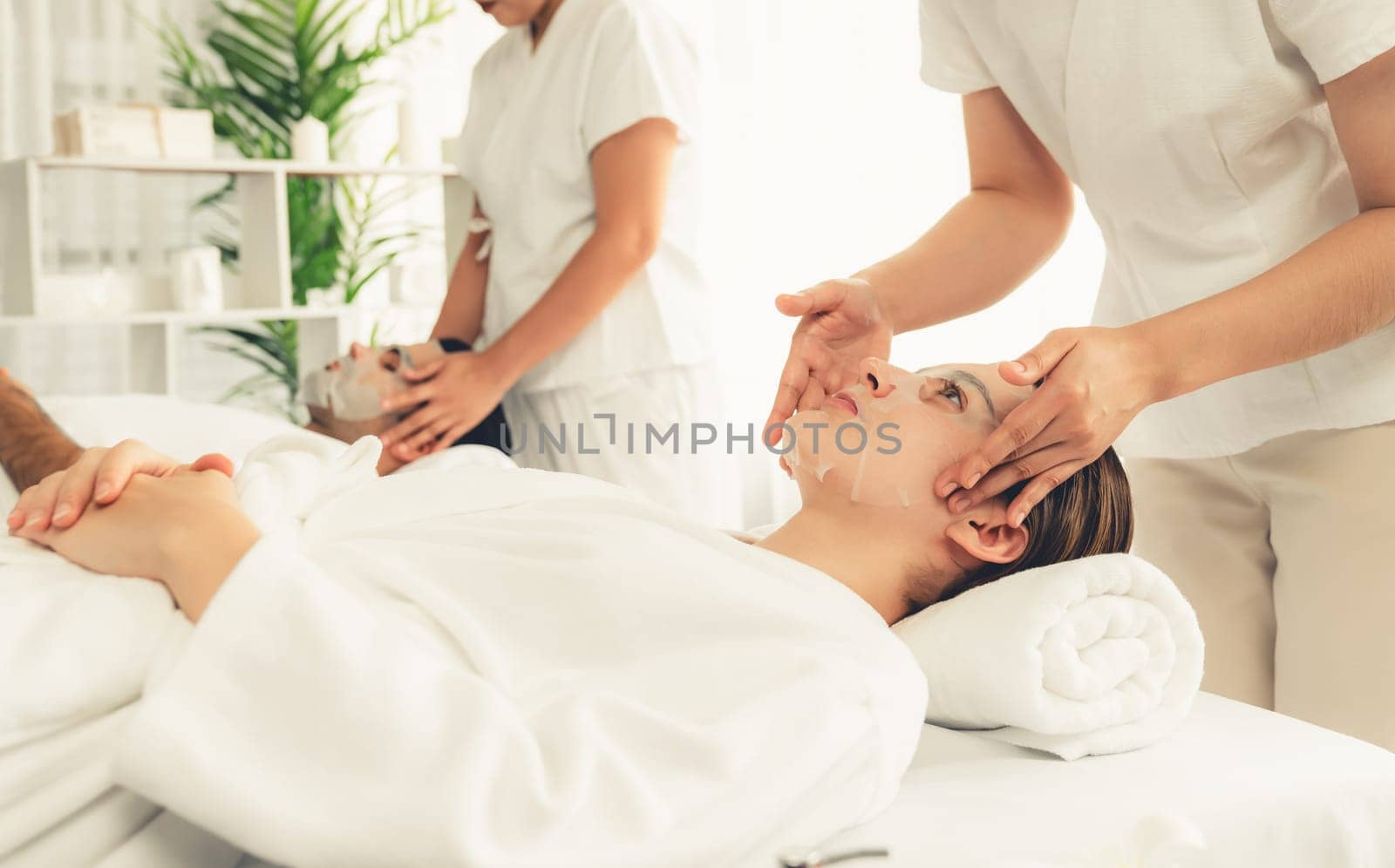 Serene modern daylight ambiance of spa salon, couple customer indulges in rejuvenating with facial skincare mask. Facial skin treatment and beauty cosmetology procedure for face. Quiescent