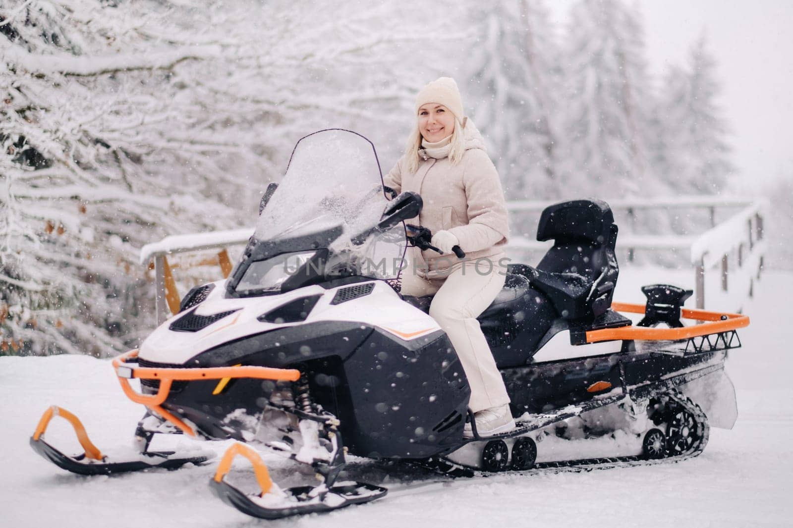 A cheerful woman rides a snowmobile in a winter forest.