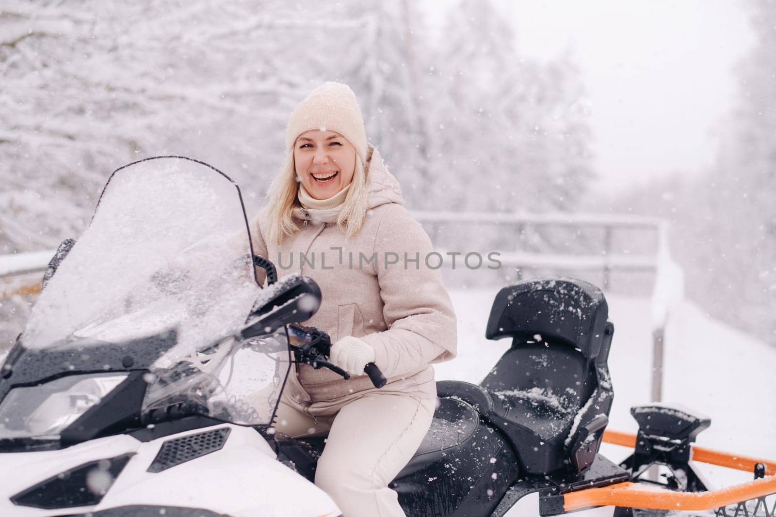 A cheerful woman rides a snowmobile in a winter forest.