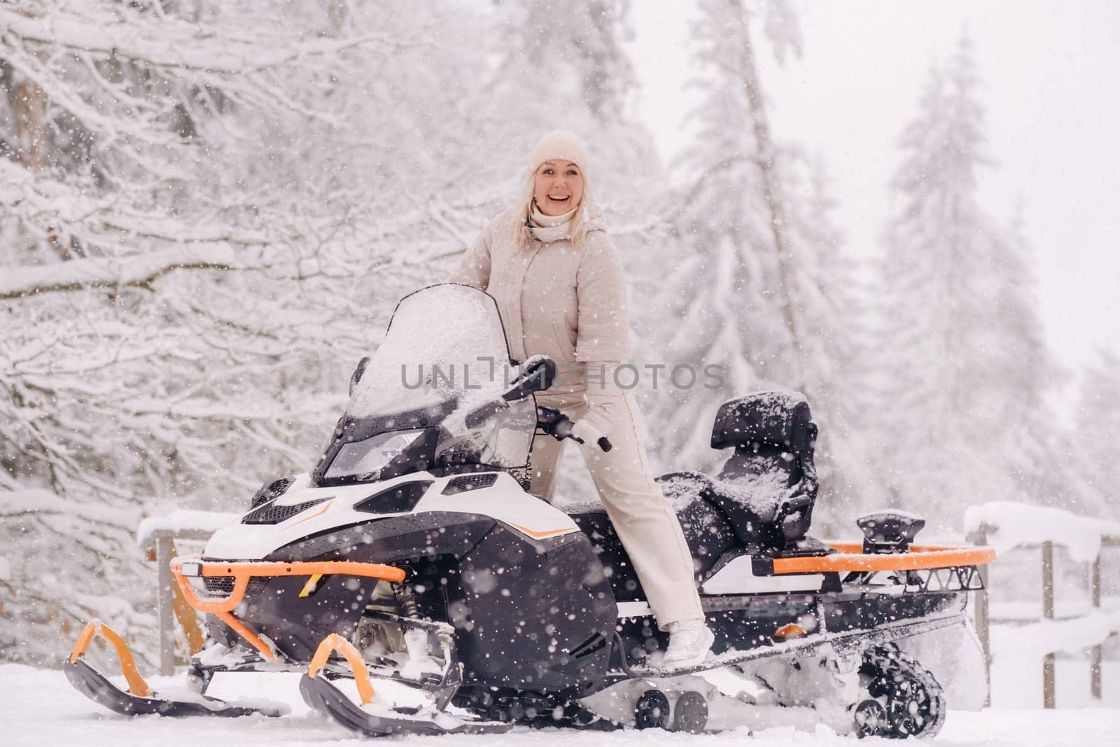 A cheerful woman rides a snowmobile in a winter forest.