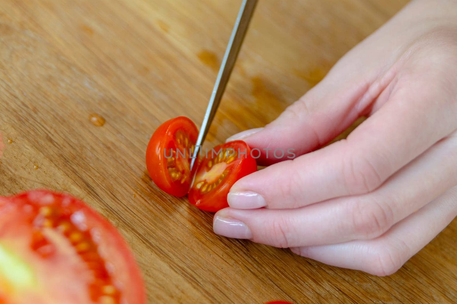 A hand cuts a cherry tomato with a knife close-up. Preparing salad to set the table. High quality photo
