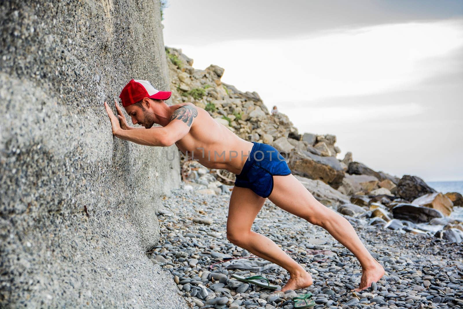 A shirtless muscular man doing stretching exercise on the beach