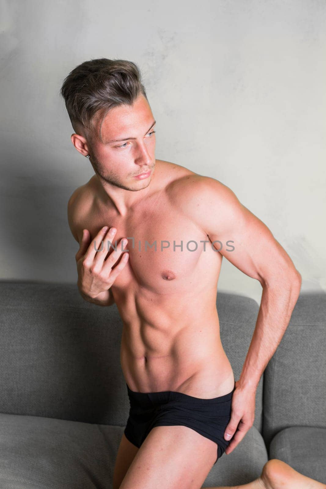 A shirtless man in black underwear sitting on a couch