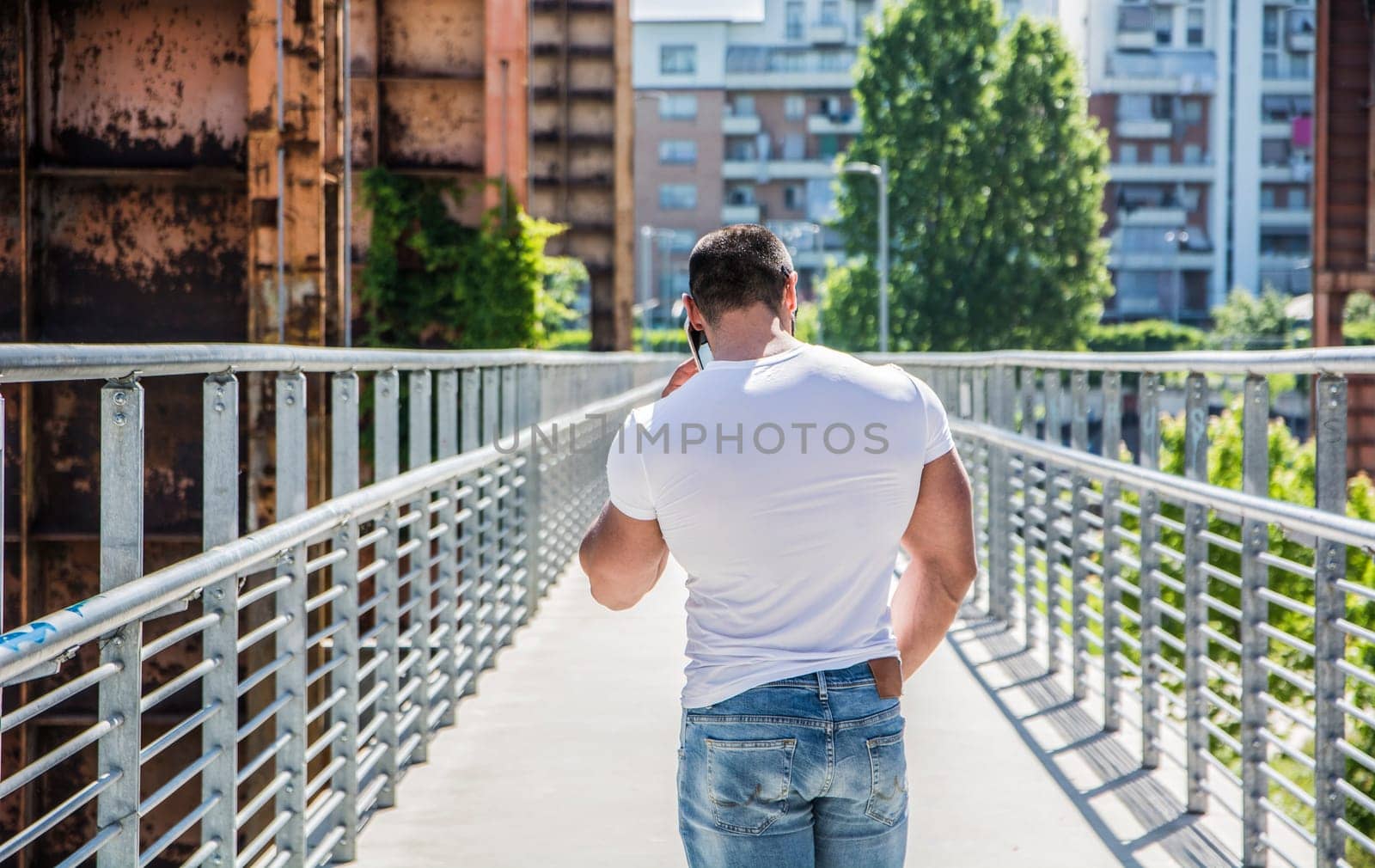 A man walking across a bridge talking on a cell phone