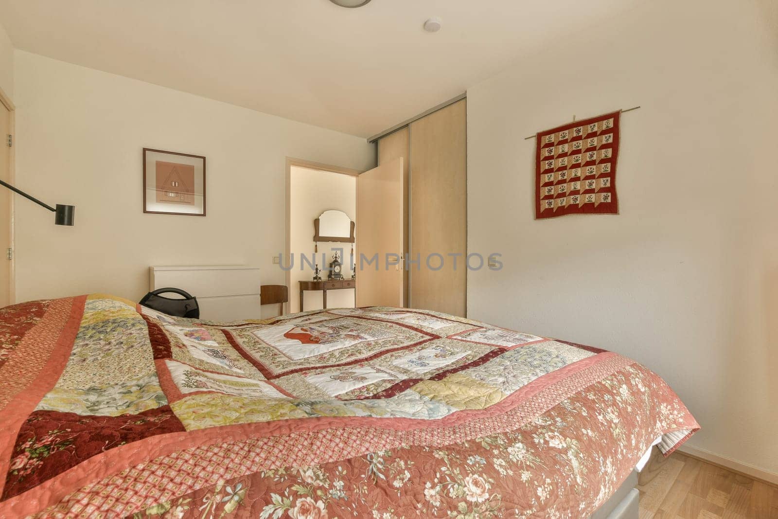 a bed with quilts on it in a room that has white walls and wood flooring around the headboard