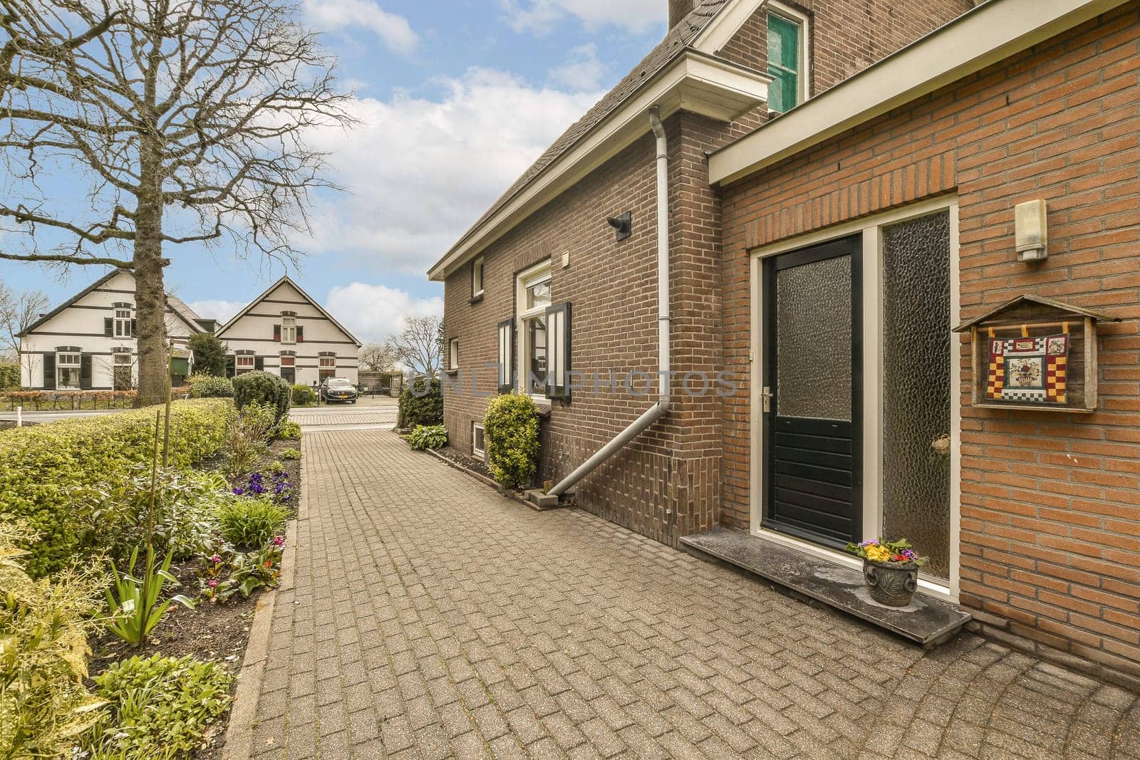 a brick house with flowers in the front and trees on the other side of the house, as seen from the sidewalk