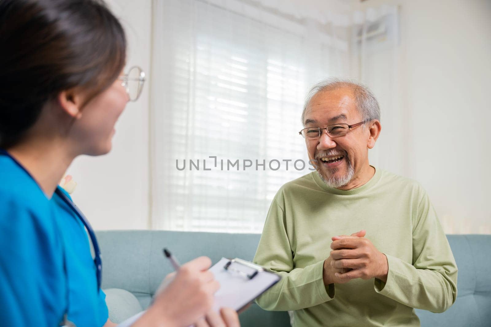 Asian young nurse writing prescription during home visit sick elder old man by Sorapop