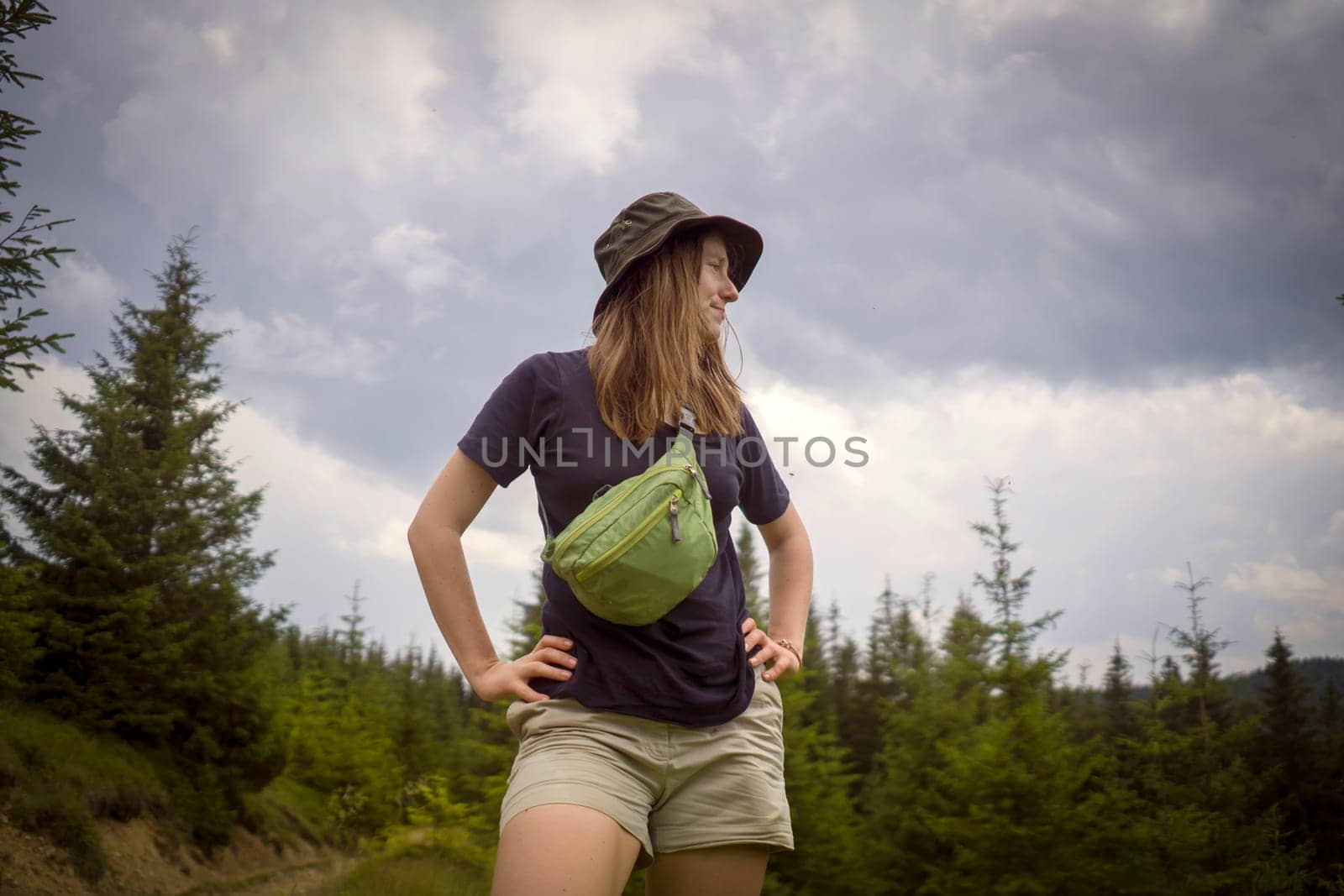 The girl walks in the mountains and the forest, a traveler is spending time active and enjoying tourism, hiking and trekking outdoors, a woman holds her waist bag.