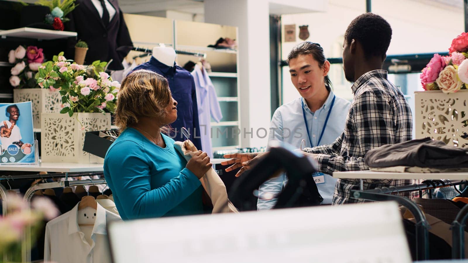 African american customers asking for employee help, explaining clothes fabric during shopping session in modern boutique. Cheeful couple shopping for fashionable merchandise in clothing store