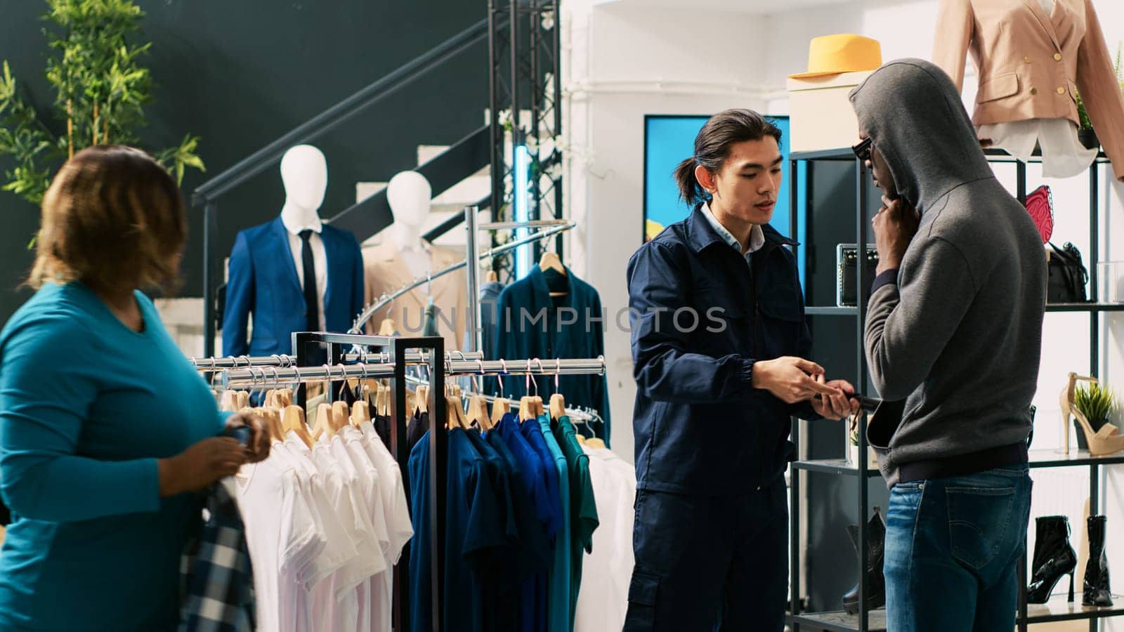 Thief trying to stole trendy clothes from modern boutique, being caught by asian bodyguard. African american couple arguing with store worker and security guard, trying to escape crime accusation