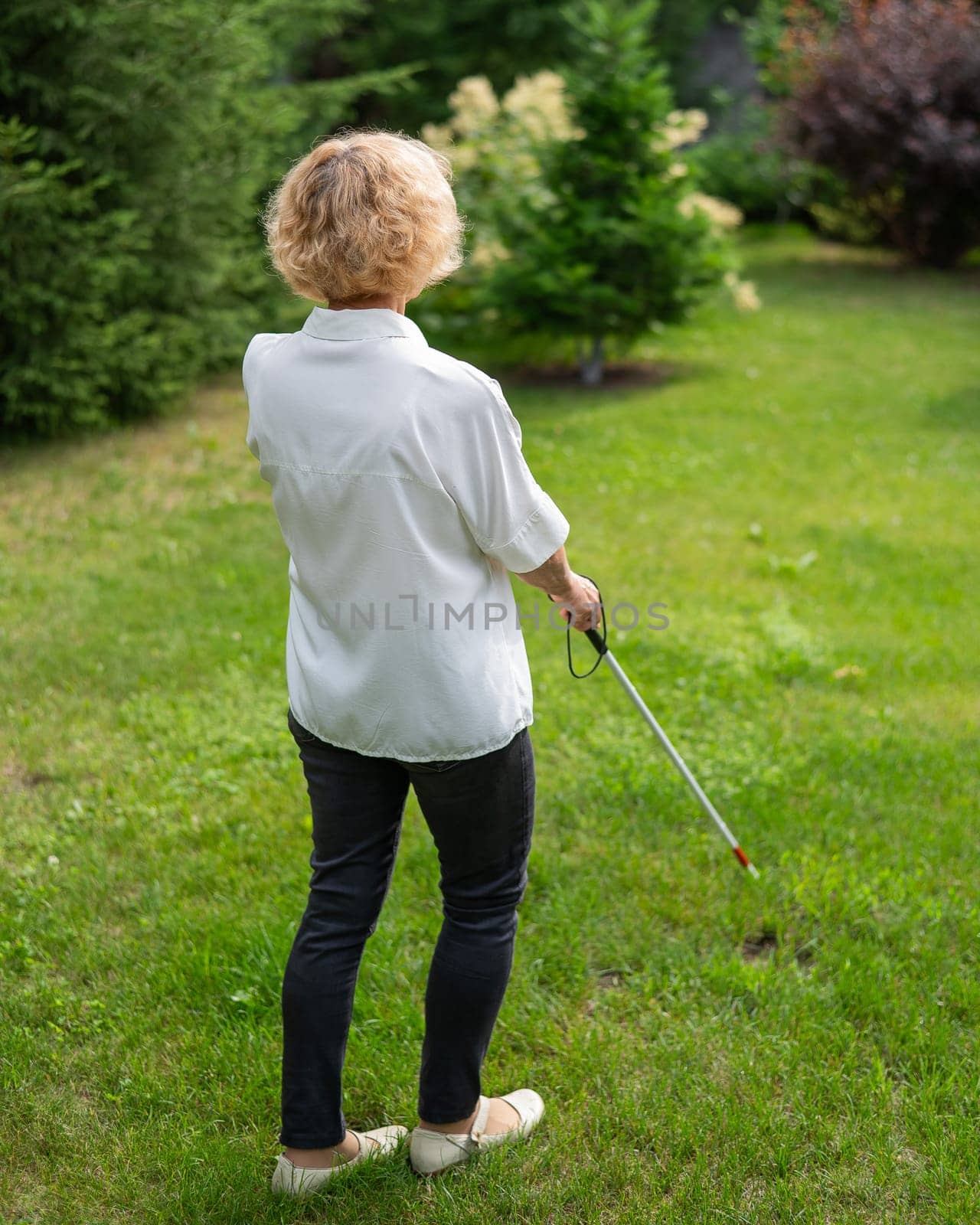 Rear view of an elderly blind woman walking in the park with a tactile cane