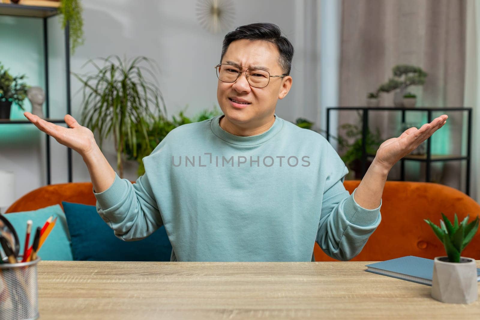 I don't know what to say. Confused Asian Japanese man feeling embarrassed about ambiguous question, having doubts, no idea, being clueless and uncertain. Middle-age Chinese guy at home room on couch