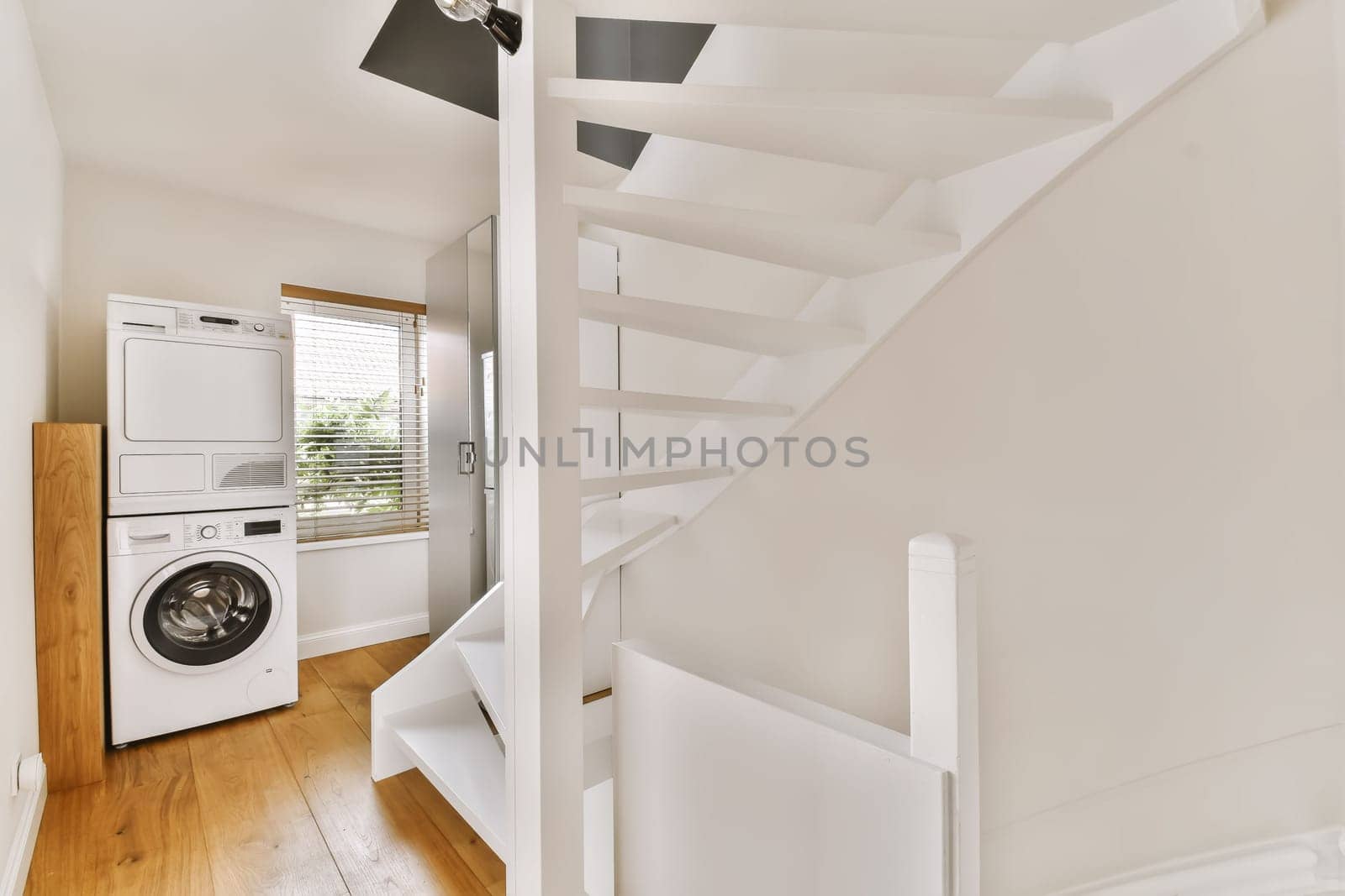 a laundry room with white walls and wood flooring, an open staircase leading up to the upper landing area