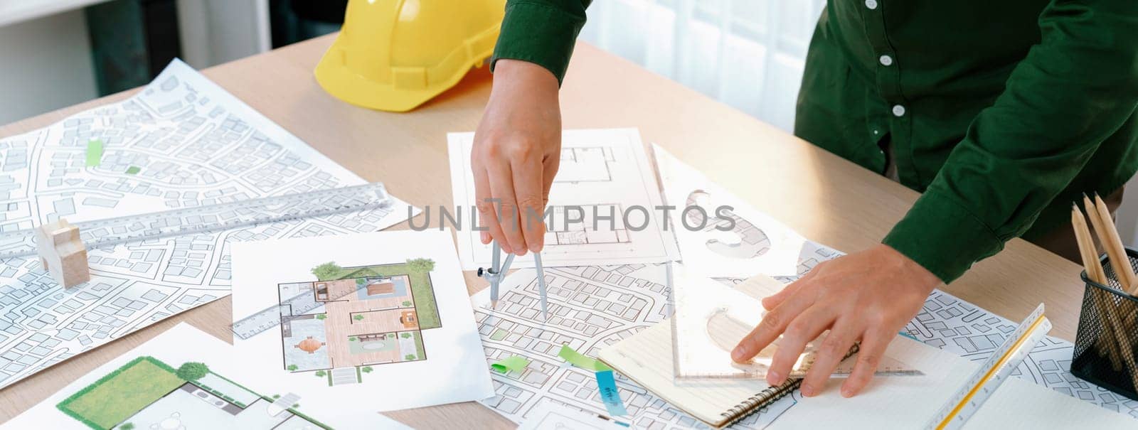 A portrait of architect using divider to measure blueprint. Architect designing house construction on a table at studio, with architectural equipment scattered around. Focus on hand. Delineation