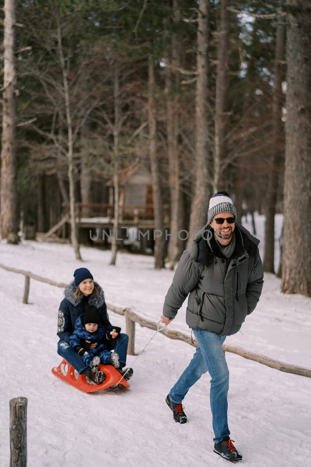 Smiling dad pulling mom and little son on a sleigh through a snowy forest. High quality photo