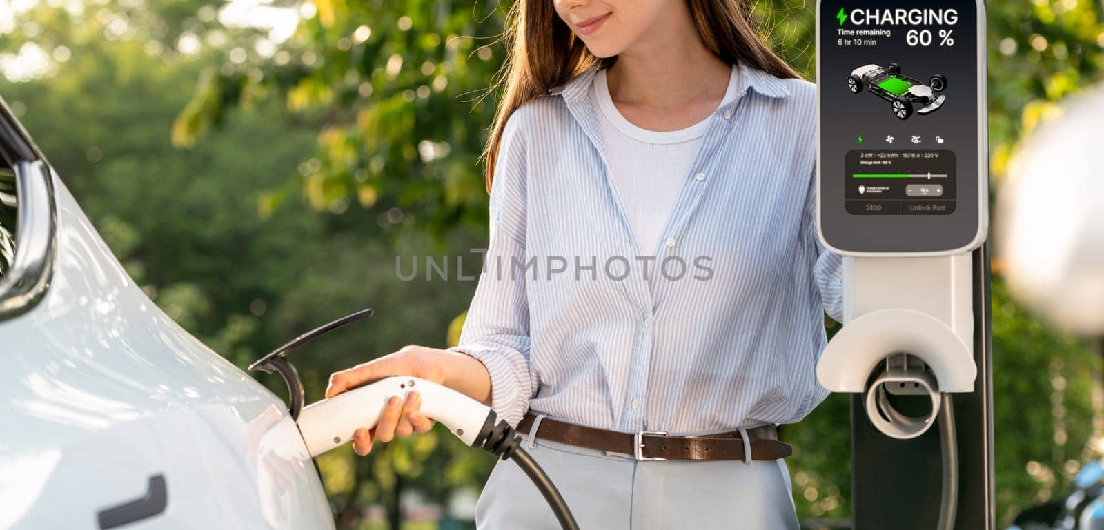 Young woman recharging battery for electric car during road trip. Exalt by biancoblue