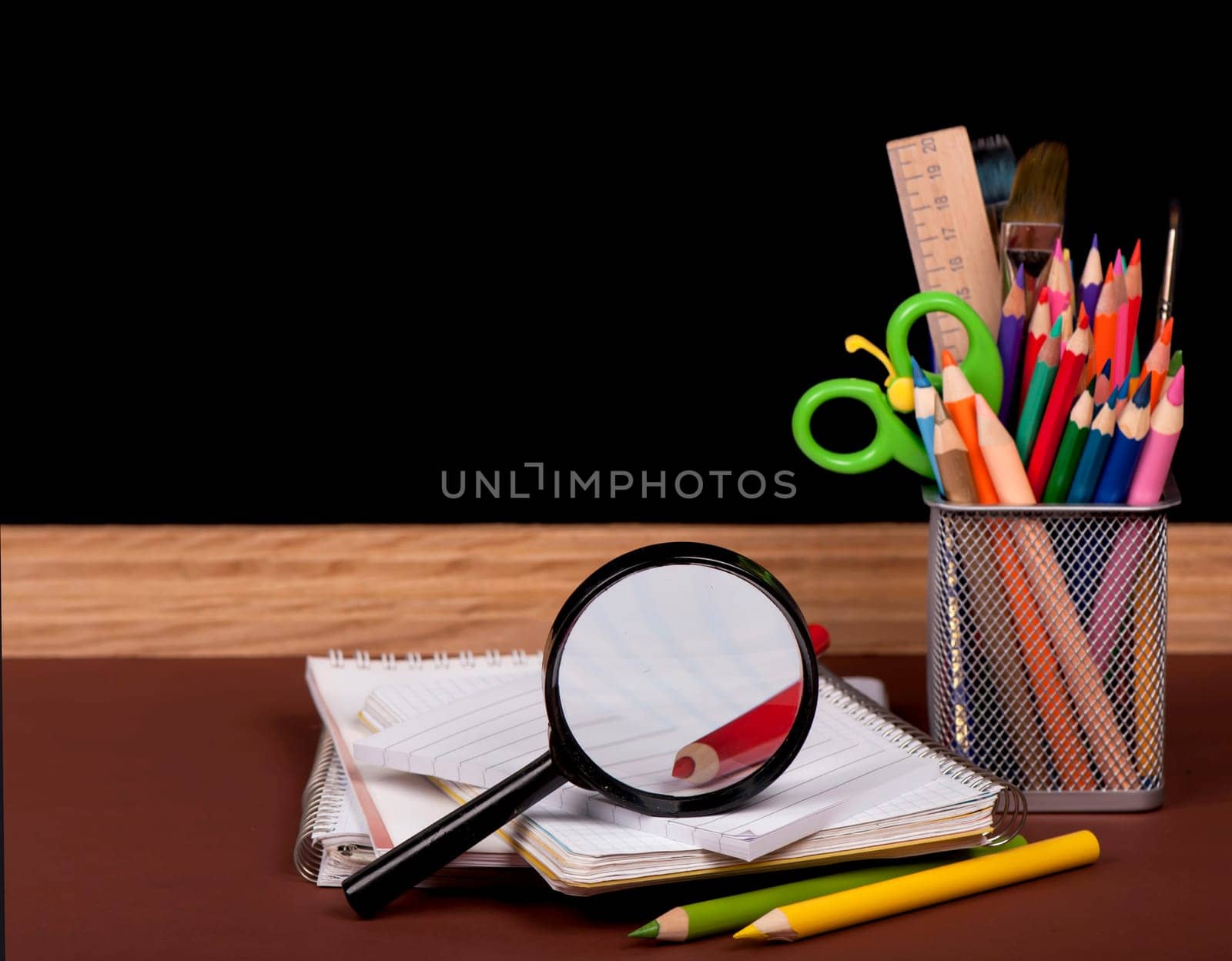 Magnifying glass, scissors, colored paper, textbooksboard, books, pencils, opened empty notebook against a dark background by aprilphoto