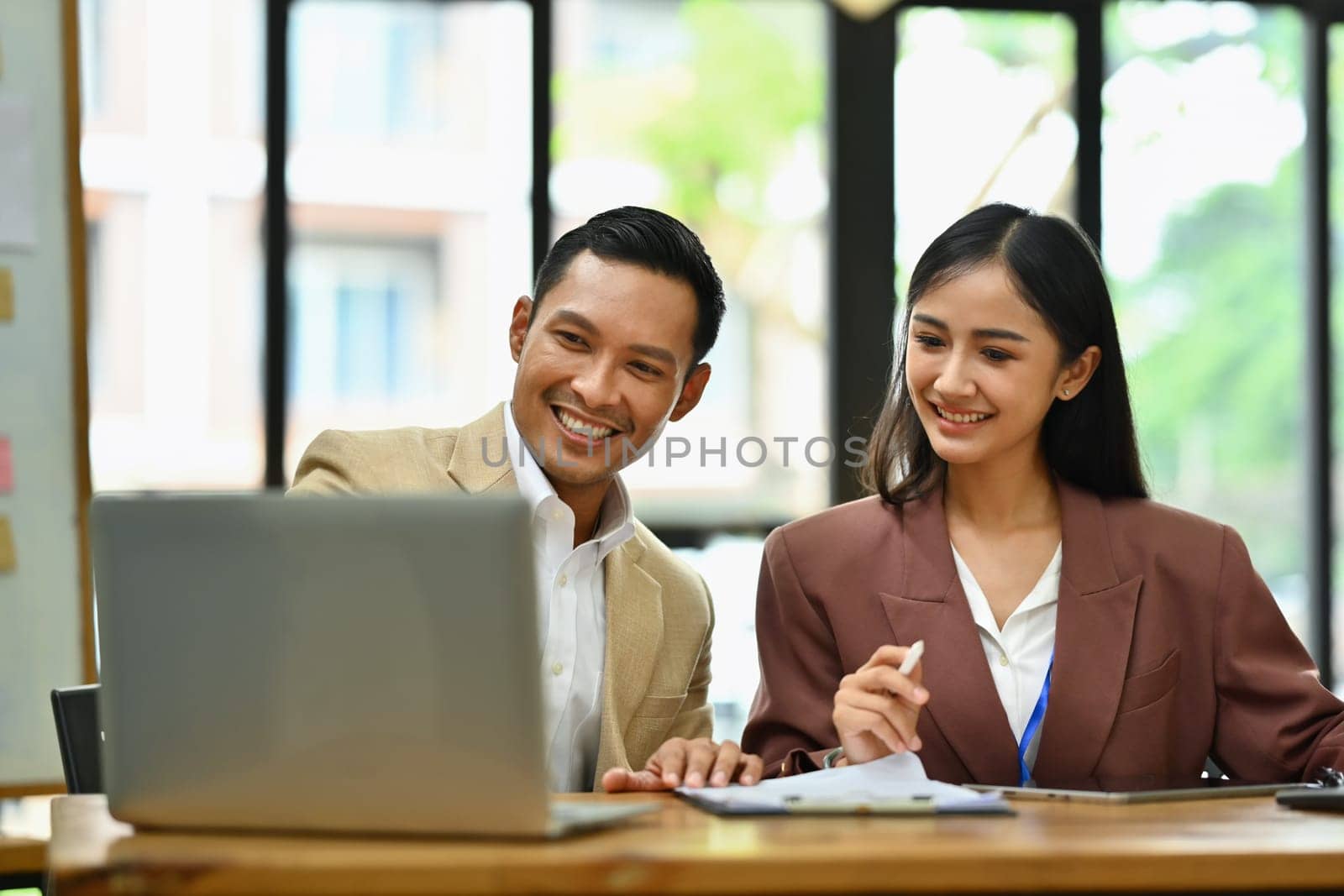 Smiling male and female employee are discussing project planning and advising on financial data report at workplace by prathanchorruangsak