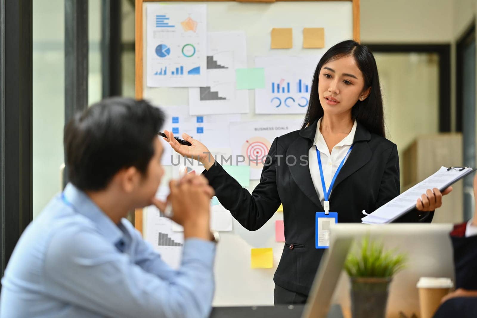 Asian female employee standing in front of flip chart giving presentation at meeting by prathanchorruangsak