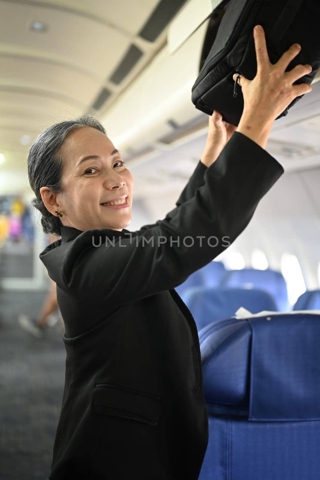 Smiling middle age woman passengers putting her luggage into the overhead compartment on an airplane.