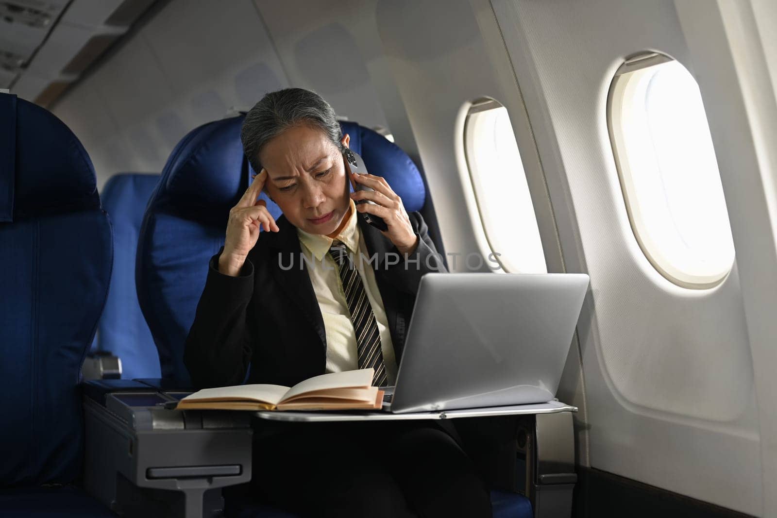 Positive middle aged businesswoman calling business contact during flight..