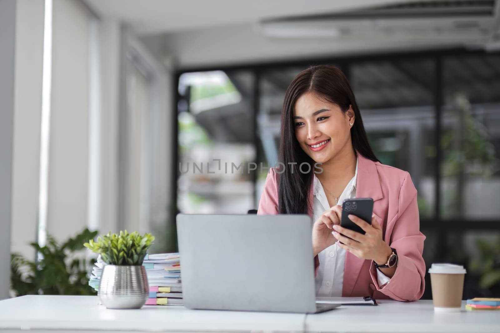 Young businesswoman using phone while sipping coffee in office..