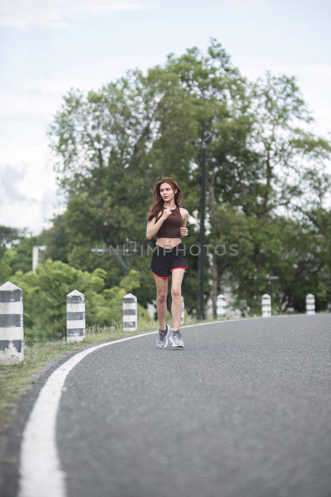 Young sporty woman jogging in the green park in the evening by wichayada