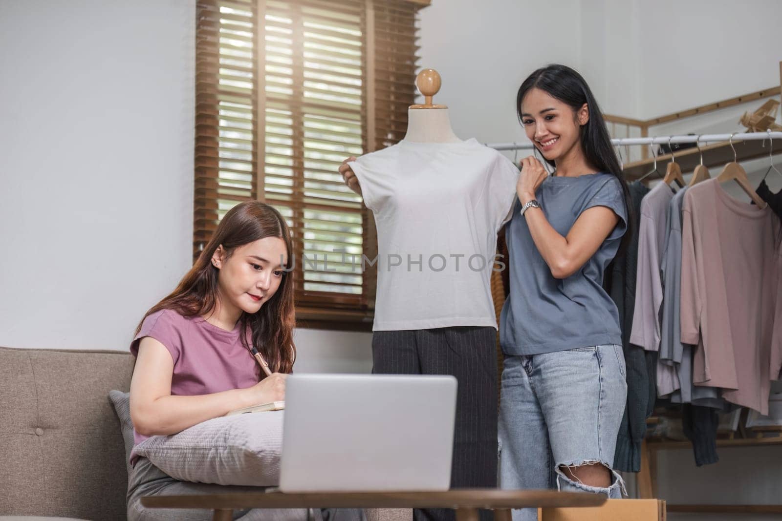 Asian couple chatting livestream to sell clothes and showing clothes to customers while selling at home..