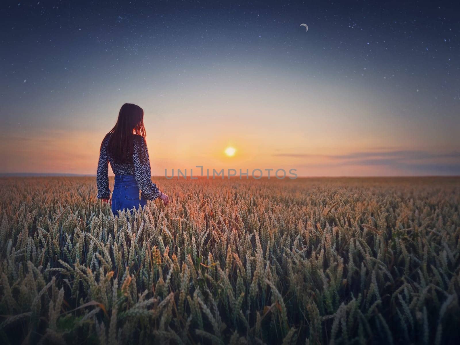 Young woman in the golden wheat field at sunset. Beautiful twilight scenery under the summer sun and crescent moon with starry sky by psychoshadow