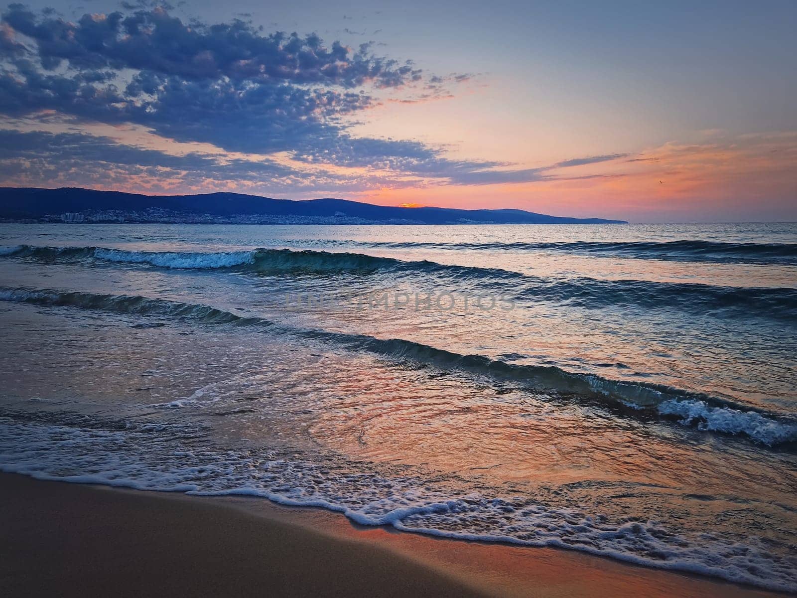 Sunrise at the sea with foamy waves on the sand and colorful sky at the horizon. Summer and travel background, Sunny Beach coastline in Bulgaria