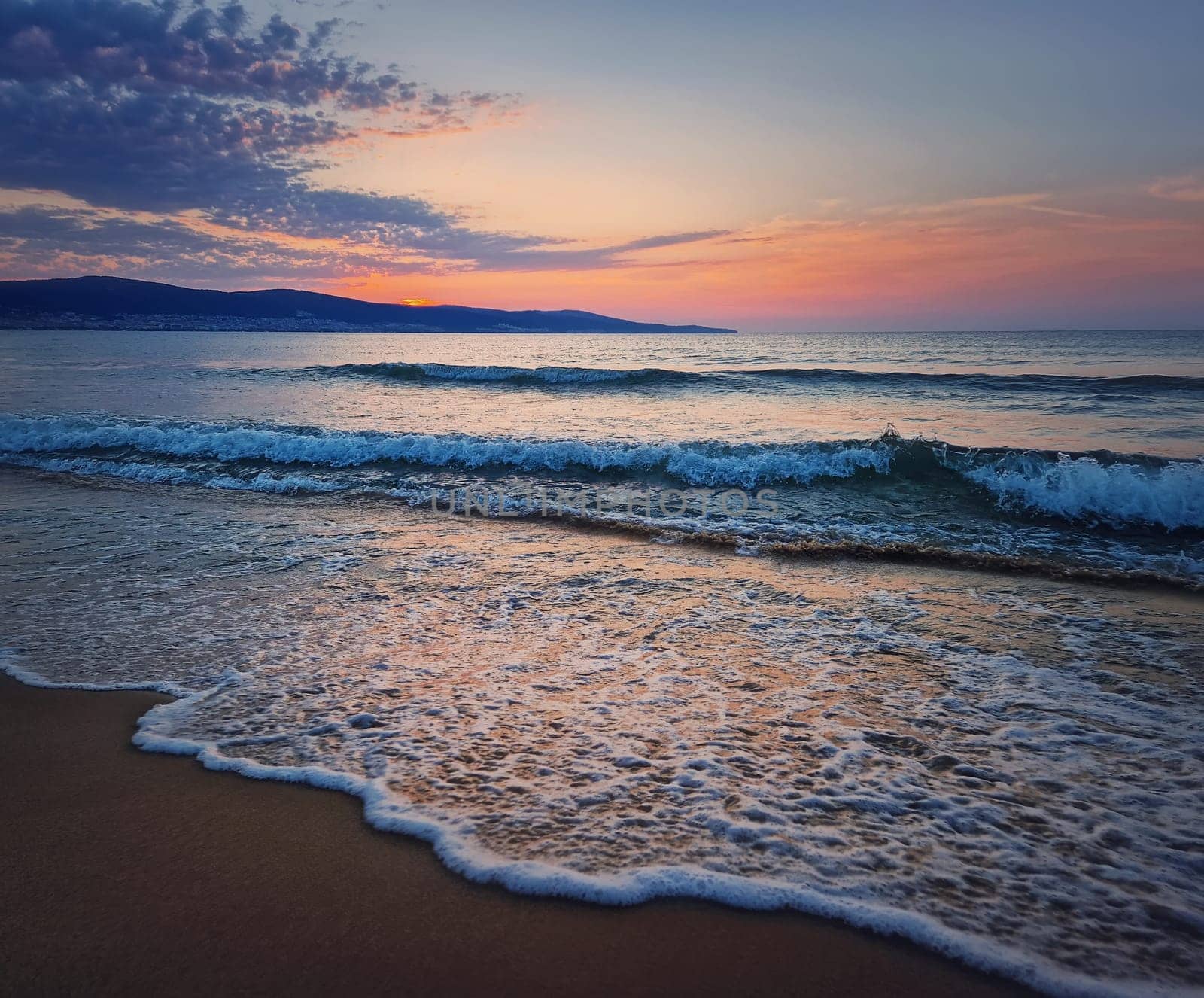 Dawn at the sea with foamy waves on the sand and colorful sky at the horizon. Sunny Beach coastline in Bulgaria. Summer and travel background by psychoshadow