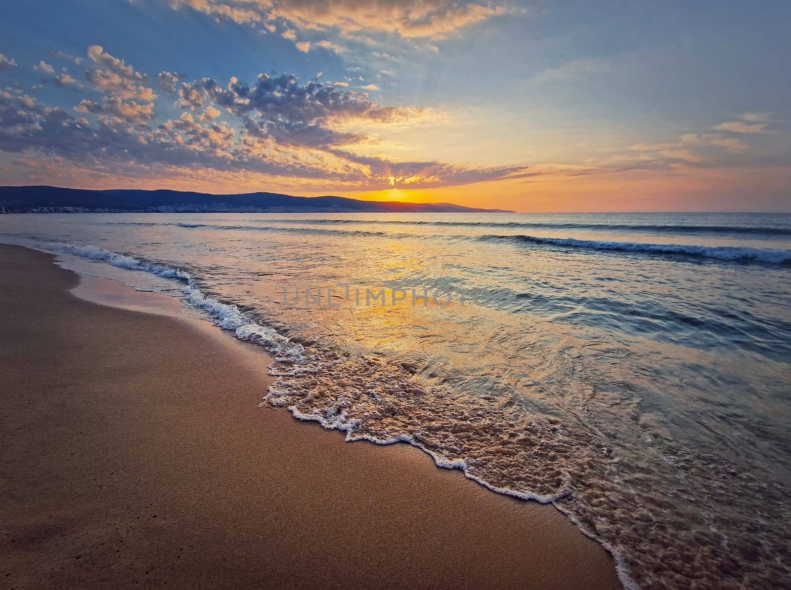 Sea sunrise scene, natural background. Early morning on the beach with a peaceful view to the dawn above the hills. Summer holiday seaside, travel concept