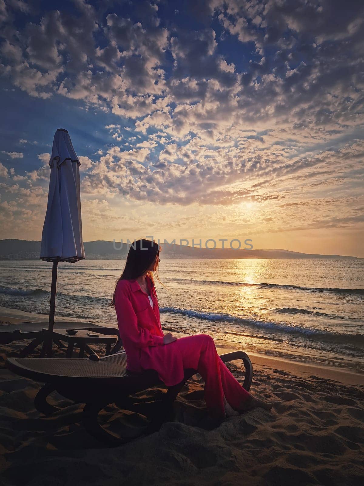 Woman relaxing on the sunbed as meets the dawn at the beach. Beautiful sea sunrise scene, summer vacation seaside, travel and holiday relaxation concept
