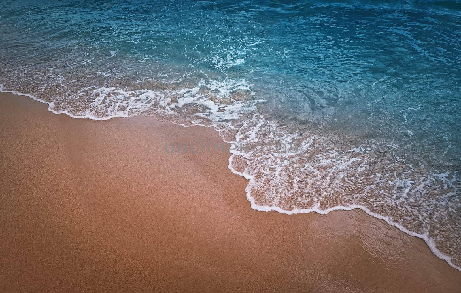 Serene blue sea with foamy waves hits the sandy shore. Beach and water texture, moody vertical background. Summer vacation seaside, holiday recreation concept