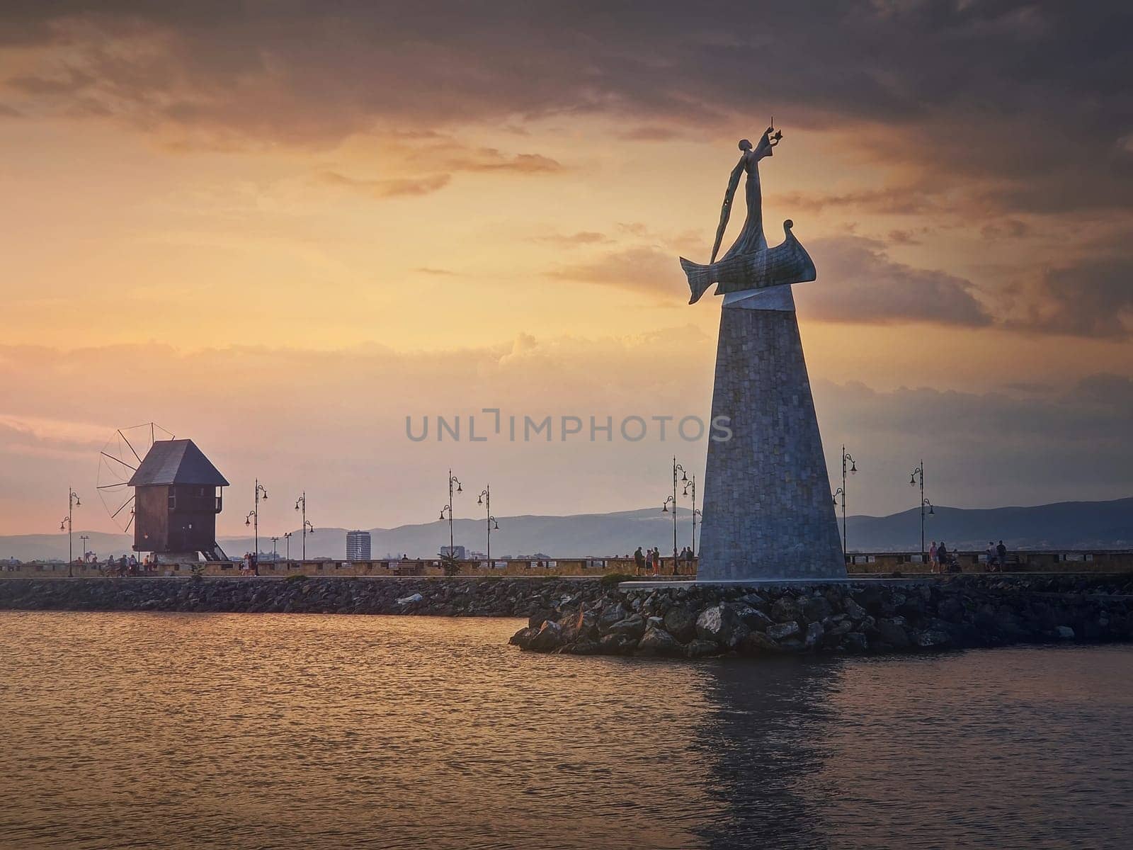 Statue of Saint Nicholas the patron of sailors, in the old town of Nessebar, Burgas, Bulgaria. Sunset scene at the coastline with a beautiful view to the big monument and the mill near the harbor